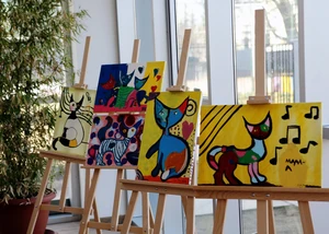Auf mehreren Staffeleien stehen vier gemalte Bilder von bunten Katzen