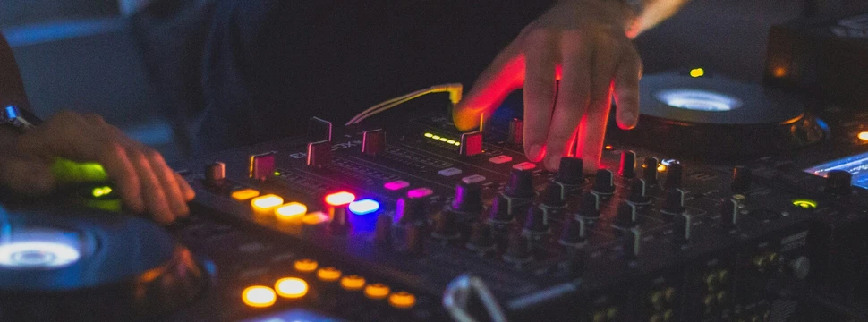 DJ-Hände an einem beleuchteten Mischpult in einem dunklen Club.