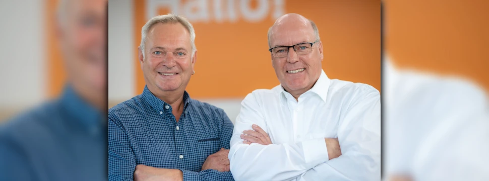 Zwei Männer mittleren Alters vor einer orangenen Wand