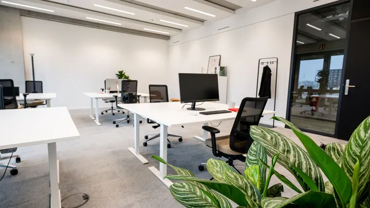 Galerie-Bild 2: Modernes Großraumbüro mit weißen Schreibtischen, schwarzen Bürostühlen und grünen Pflanzen im Vordergrund