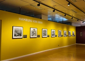 Acht gerahmte Bilder hängen an einer gelben Wand mit der Überschrift "Hamburg von oben"