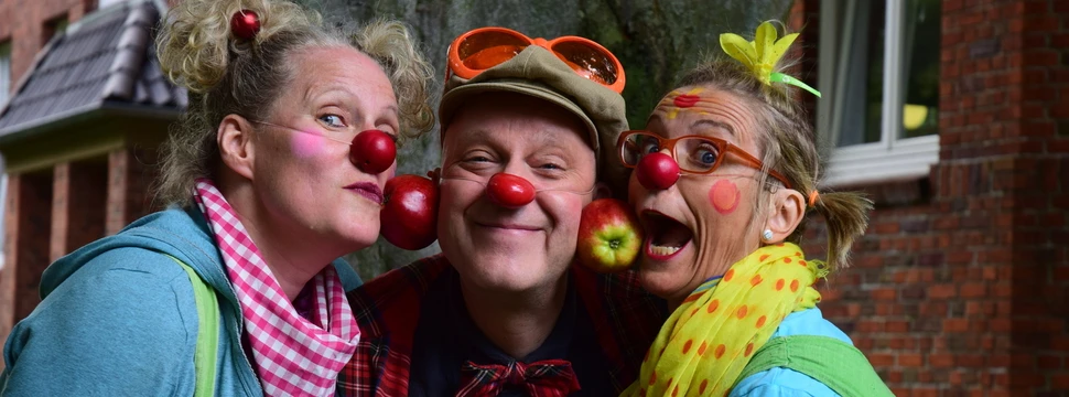 Drei lustige Clowns, die mit ihren Wangen Äpfel halten.