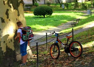 Ein Junge steht mit seinem Schulranzen und Fahrrad vor einem Baum