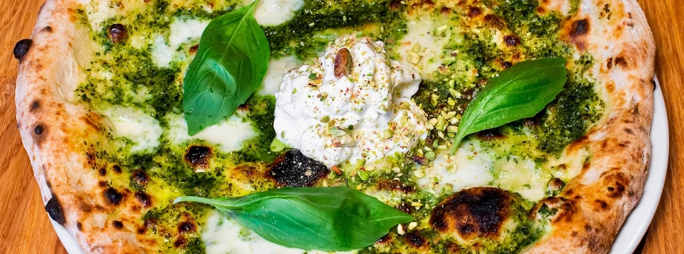 Pizza mit grünem Pesto, weißem Burrata-Käse und frischen Basilikumblättern auf Holztisch.