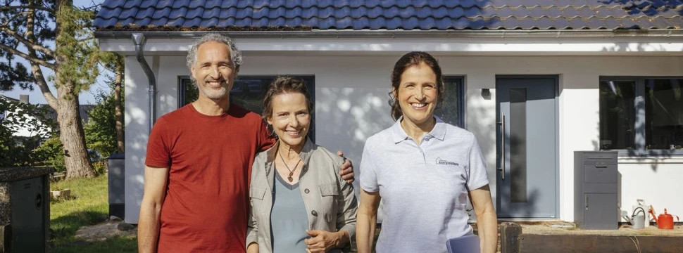 zwei Frauen und ein Mann stehen vor einem weißen Haus