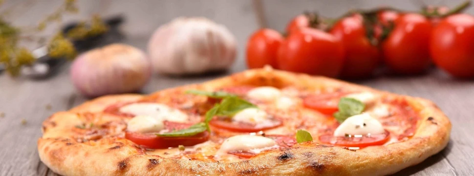 Knusprige Pizza mit Tomaten und frischen Basilikum, im Hintergrund Tomaten und Knoblauch