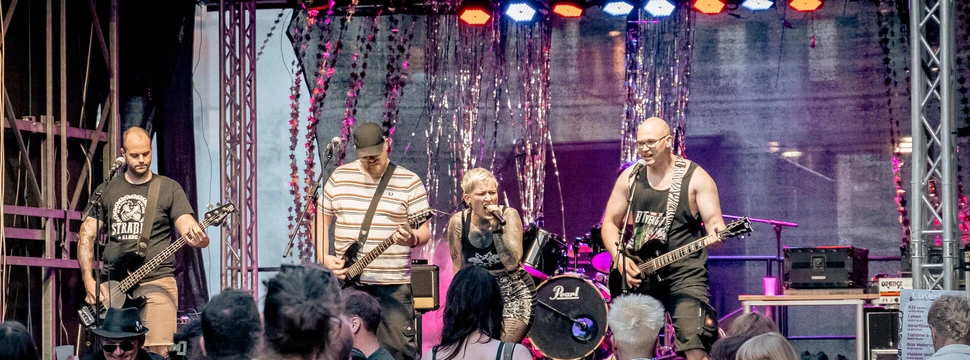Ein Band ist auf der Bühne. Vor der Bühne sind einige Mensche