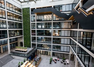 Modernes Büroatrium mit mehrstöckigen Glasfassaden, grüner Wand und Lounge-Bereich im Erdgeschoss.