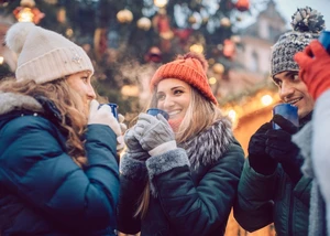 zwei Frauen und ein Mann mit Winterkleidung und Mützen trinken Glühwein