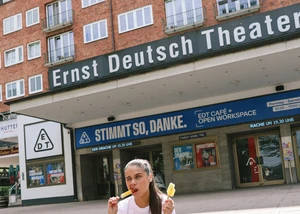 Ein Mädchen sitzt Eis essend vor dem Ernst Deutsch Theater