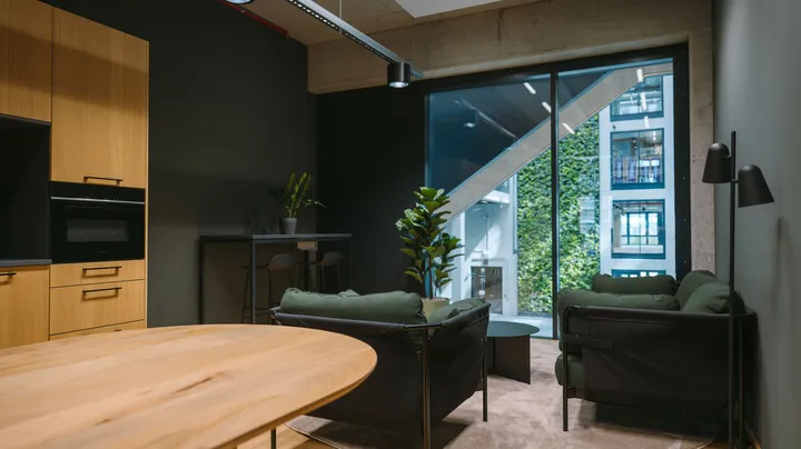 Galerie-Bild 2: Modernes Büro mit Holzküche, grünen Lounge-Sesseln und großen Fenstern zum begrünten Innenhof.