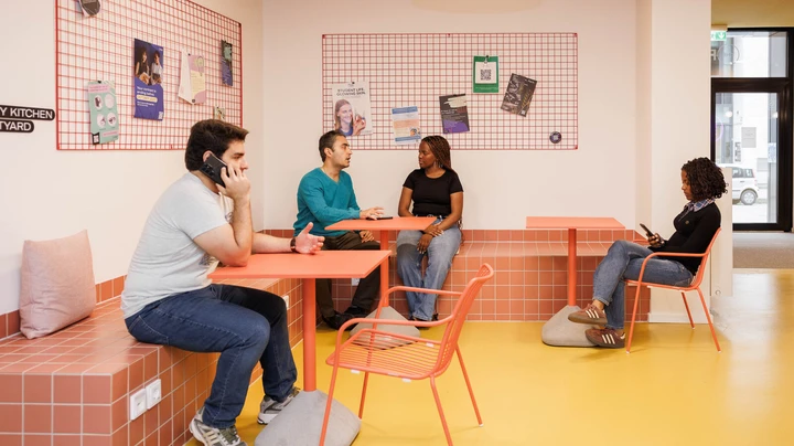 Galerie-Bild 8: Studierende sitzen auf bunten Sitzmöbeln, einer telefoniert