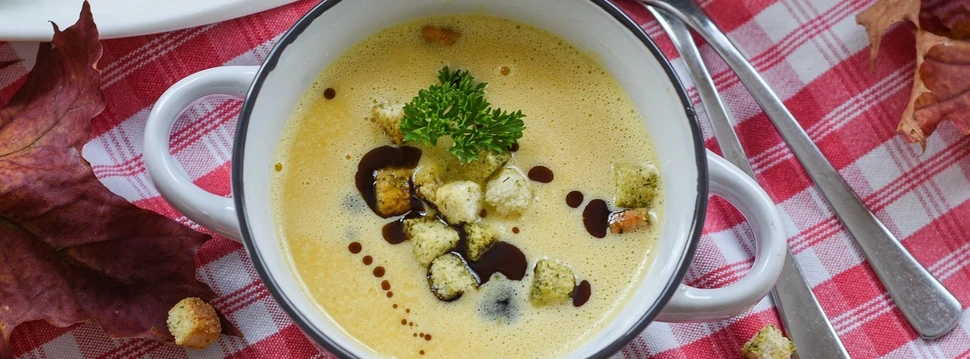 kleiner Topf mit Suppe und Croutons auf einer rot karierten Tischdecke