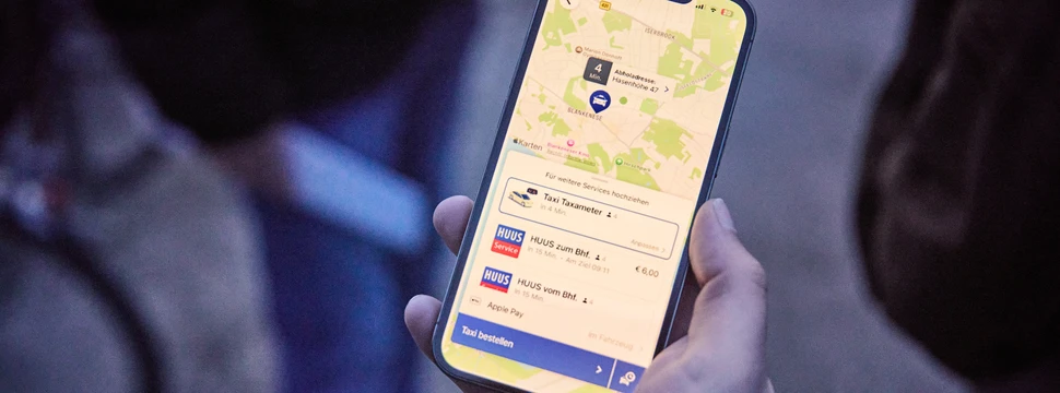 Eine Hand hält ein Smartphone, auf dem das Mobilitätsangebot HUUS geöffnet ist