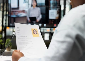 Eine Person mit einem Blatt Papier in der Hand, die an einem Tisch sitzt