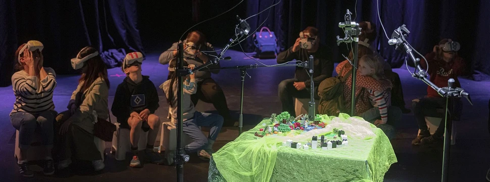 Fundus Theater Hamburg Aufführung mit Kindern und Jugendlichen, die VR-Brillen tragen und um einen grün beleuchteten Tisch mit interaktiven Elementen sitzen - experimentelles partizipatives Theater