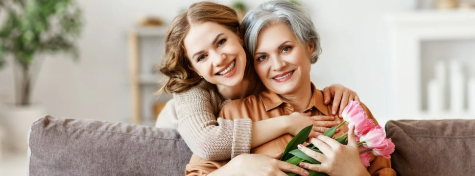 eine jüngere Frau umarmt eine ältere Frau, die einen Blumenstrauß in der Hand hat