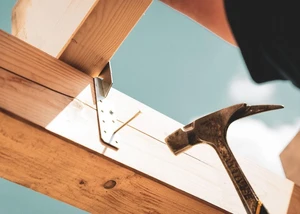 ein Zimmerer schlägt mit einem Hammer einen Nagel in einen Dachstuhl aus Holz